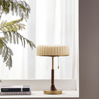 A Clérachic table lamp on a white windowsill with sheer curtains behind it, a feathery plant to the left and two books at its side.