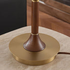 Close view of the gold metal base and turned walnut stem of this Clérachic table lamp, resting on a travertine surface.