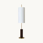 This Clérachic pleated-shade floor lamp on a plain white backdrop, a white cylinder shade on a slim brass rod over a walnut-colour base.