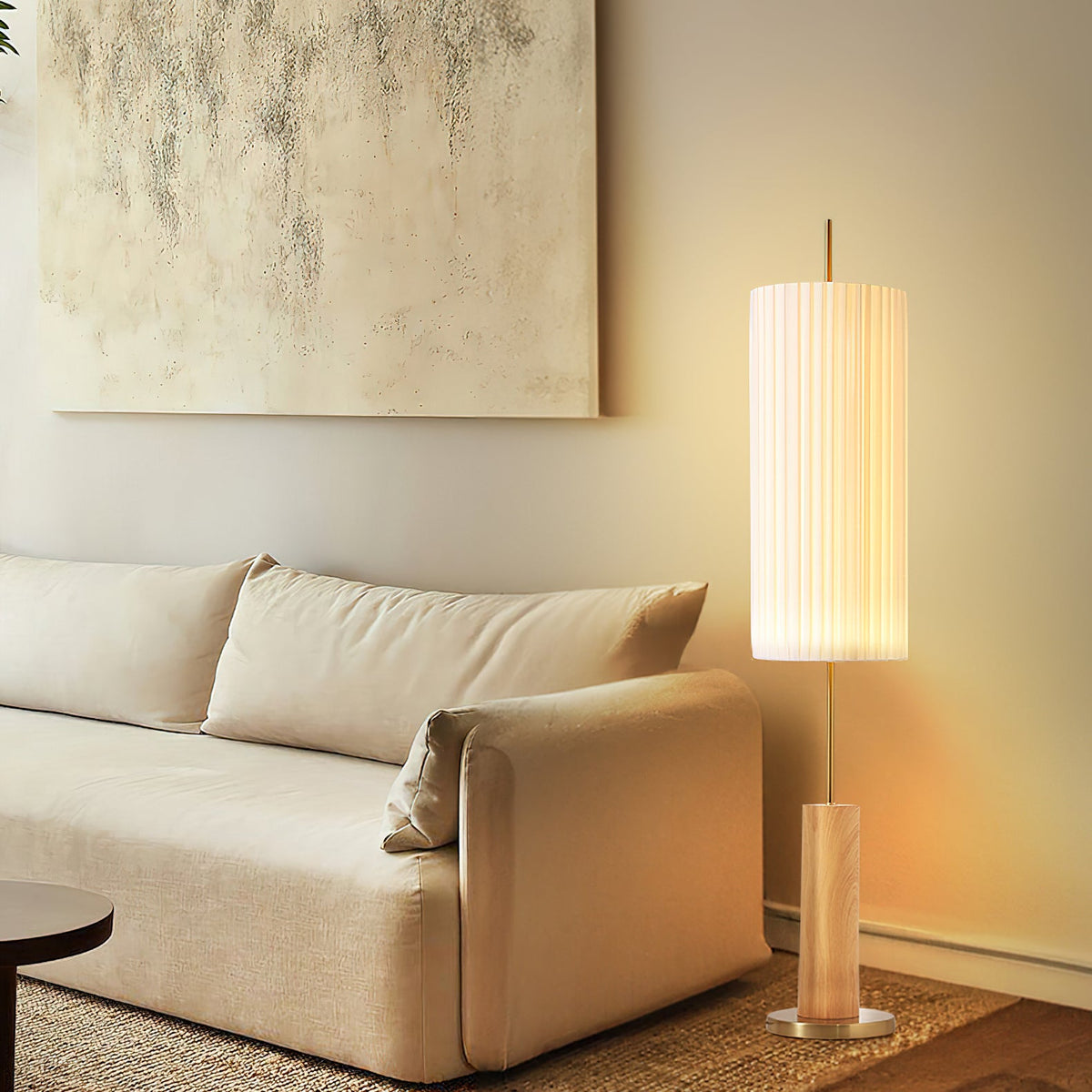 Tall Clérachic floor lamp with a wood-colour base, lit beside a cream sofa in a room with a pale textured painting.