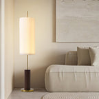 This Clérachic floor lamp with a walnut-colour base stands by a low cream sofa, with a plaster-textured artwork on the wall.