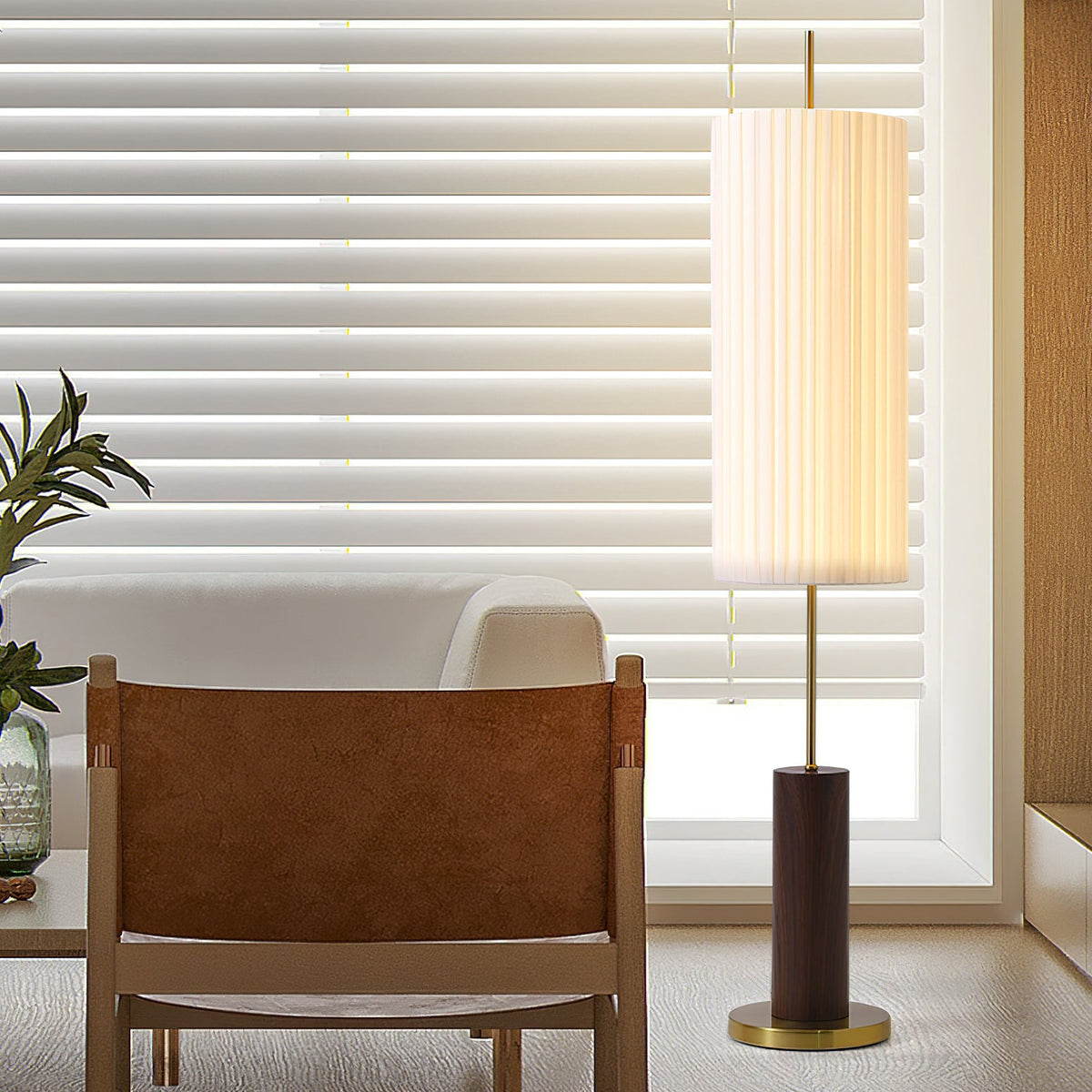 Pleated shade of this Clérachic floor lamp lit against a window with horizontal blinds, beside a tan leather and wood chair.