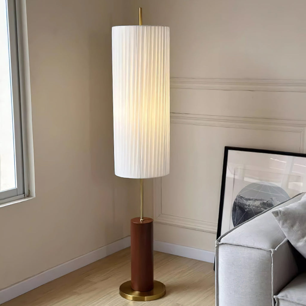 Close, low view of this Clérachic floor lamp by a window, its tall pleated shade over a warm brown base on a light wood floor.