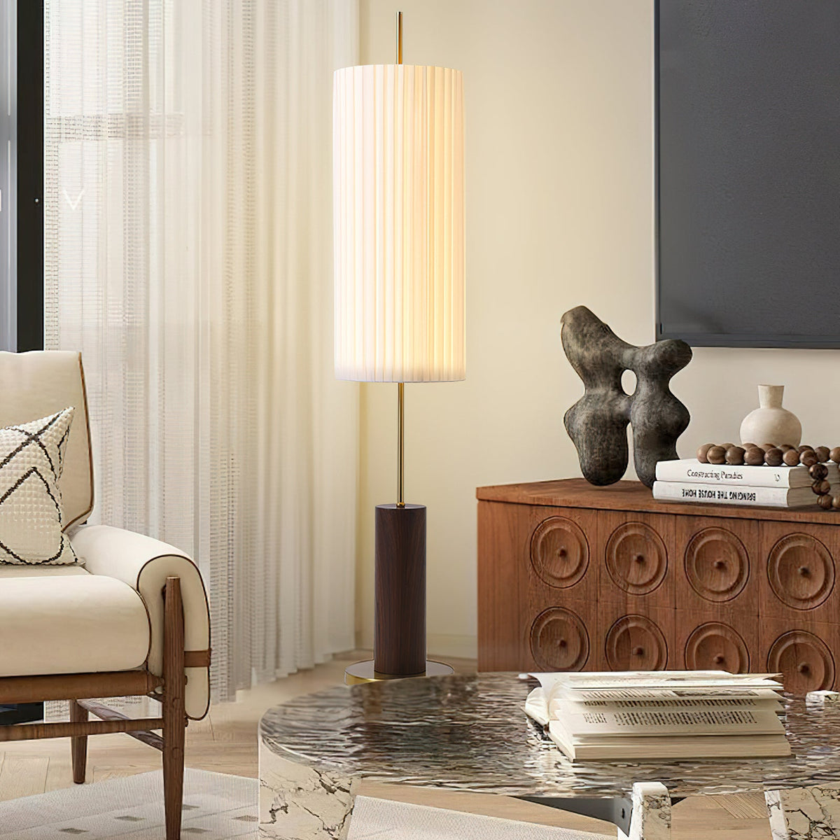 Narrow view of this Clérachic pleated floor lamp beside a cream armchair, a sculptural ornament and a rippled-glass coffee table.
