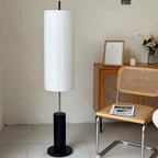 Tall Clérachic floor lamp with a black base in a plain corner, with a woven cane cabinet, a framed line drawing and a cane chair.
