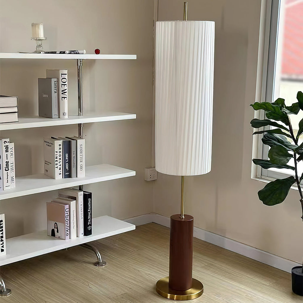 Clérachic floor lamp beside a white open shelving unit with books and a plant, its shade almost reaching the top of the frame.