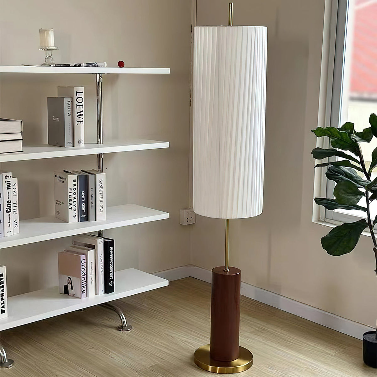 Clérachic floor lamp beside a white open shelving unit with books and a plant, its shade almost reaching the top of the frame.