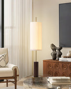 This Clérachic floor lamp beside a walnut cabinet and a wooden-framed armchair, with a glass coffee table and books in front.