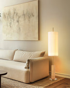 Warm-lit Clérachic floor lamp with a wood-colour base, beside a cream sofa, a round black side table and a jute rug.