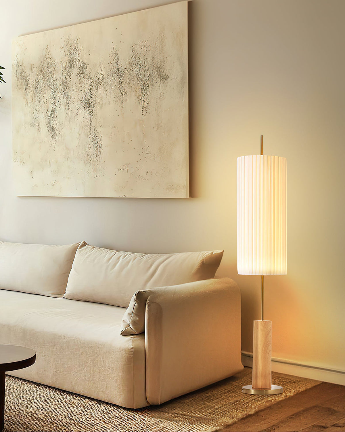 Warm-lit Clérachic floor lamp with a wood-colour base, beside a cream sofa, a round black side table and a jute rug.