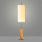 This Clérachic floor lamp with a light wood-colour base and brass foot, lit against a grey backdrop, a brass rod above the base.
