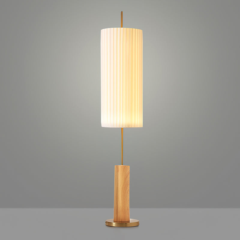 This Clérachic floor lamp with a light wood-colour base and brass foot, lit against a grey backdrop, a brass rod above the base.