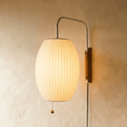 Clérachic glowing barrel-shaped pleated fabric wall lamp on a curved chrome arm with a walnut-tone mount and pull chain.