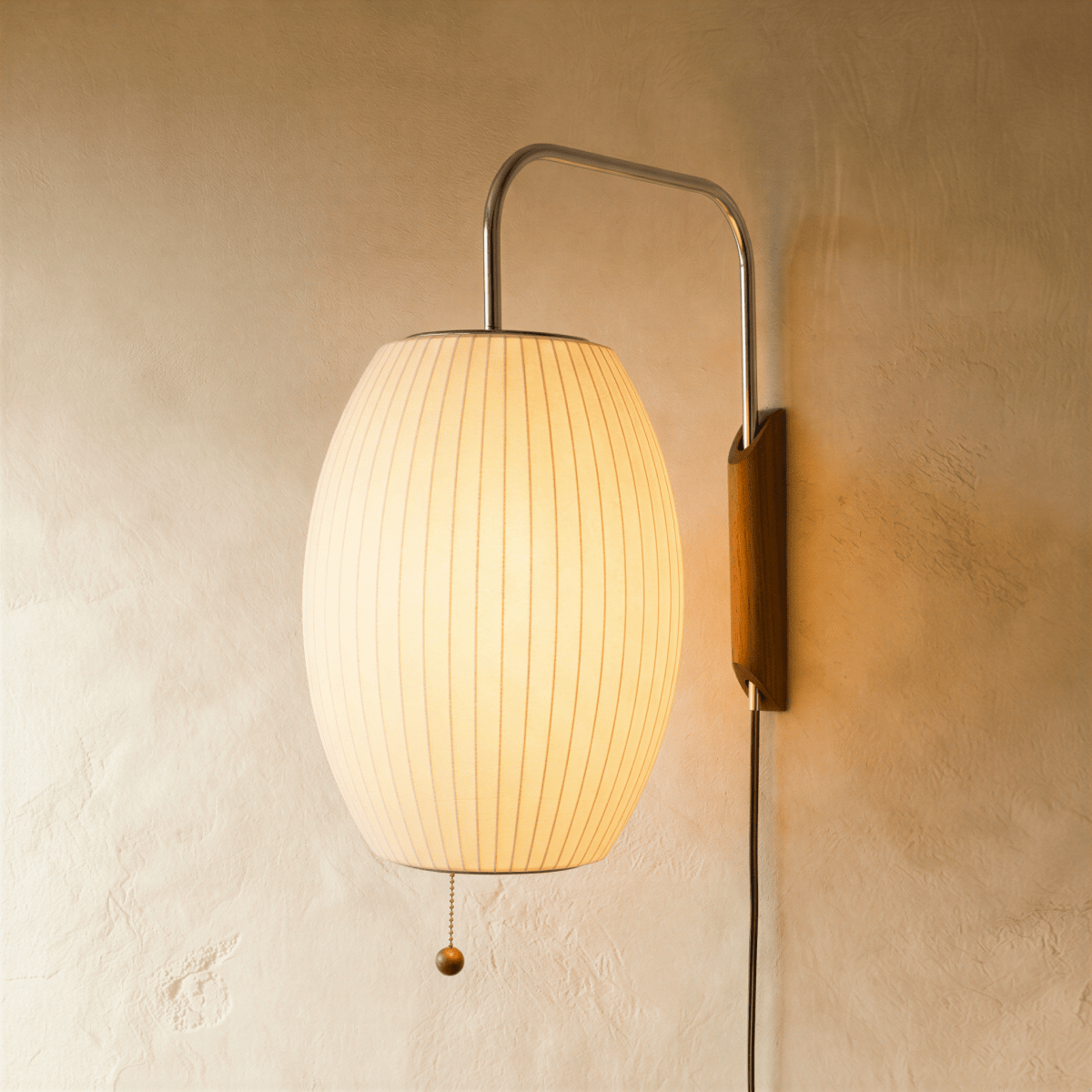 Clérachic glowing barrel-shaped pleated fabric wall lamp on a curved chrome arm with a walnut-tone mount and pull chain.