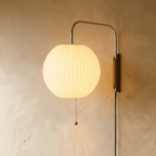 Clérachic round globe pleated fabric wall lamp glowing warmly on a chrome arm, wooden wall mount and a pull chain.