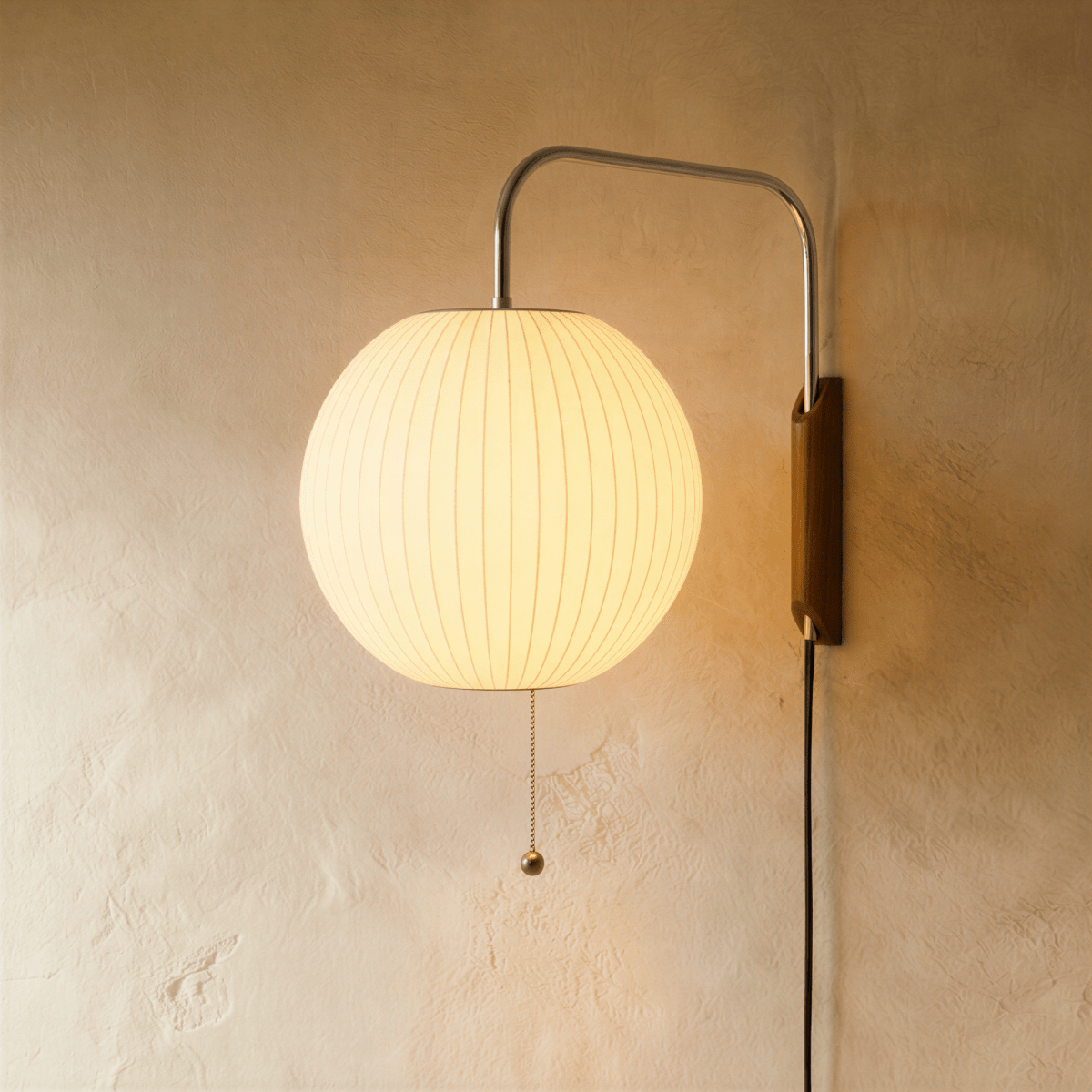 Clérachic round globe pleated fabric wall lamp glowing warmly on a chrome arm, wooden wall mount and a pull chain.