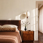 Clérachic barrel-shaped pleated wall lamp mounted beside a bed above a burr-wood bedside cabinet and a black vase.