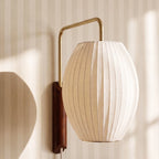 Close view of a Clérachic barrel-shaped pleated fabric shade on a brass-tone arm with a dark wood wall mount.