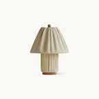 Pleated linen table lamp from Clérachic with a matching fabric base, a small wooden ball finial and a wooden foot, on white.
