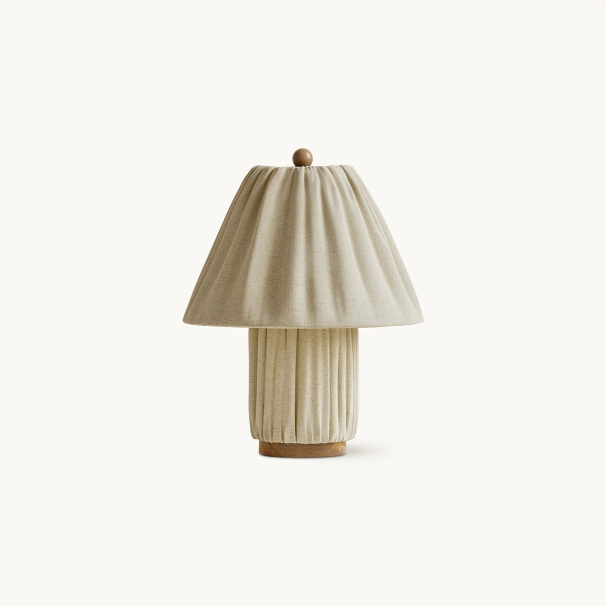 Pleated linen table lamp from Clérachic with a matching fabric base, a small wooden ball finial and a wooden foot, on white.