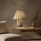 A Clérachic pleated linen lamp glows softly on a wooden console beside a stack of books and dried pampas grass.