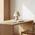 Small Clérachic pleated lamp on a pale oak desk with an open book, in a room with soft sunlight on the wall.