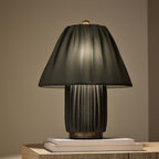 Dark charcoal version of this Clérachic pleated lamp, lit from within and resting on a pair of books on a wooden surface.