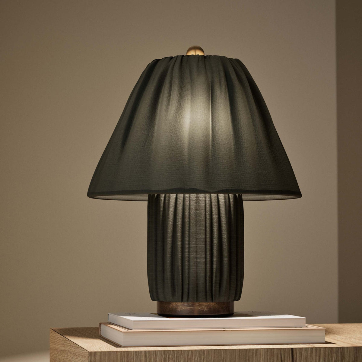 Dark charcoal version of this Clérachic pleated lamp, lit from within and resting on a pair of books on a wooden surface.