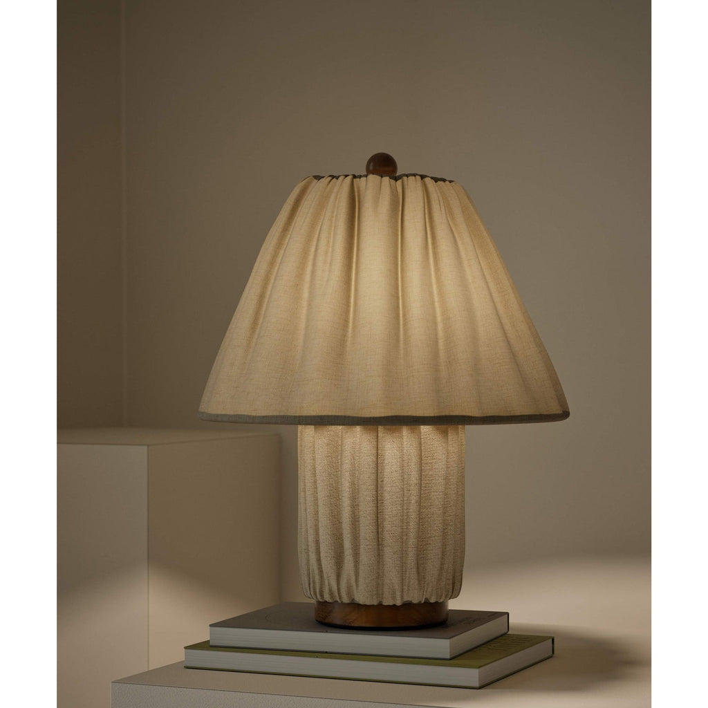 Close view of a Clérachic pleated linen lamp, its shade and base in the same fabric, on a stack of books against a taupe wall.