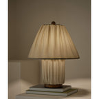 Close view of a Clérachic pleated linen lamp, its shade and base in the same fabric, on a stack of books against a taupe wall.