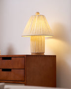 The Clérachic pleated lamp glows warm on top of a walnut sideboard with dovetailed drawers, against a pale wall.