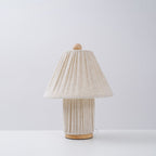 Unlit Clérachic pleated linen lamp with a wooden foot, standing on a white surface against a pale grey wall.