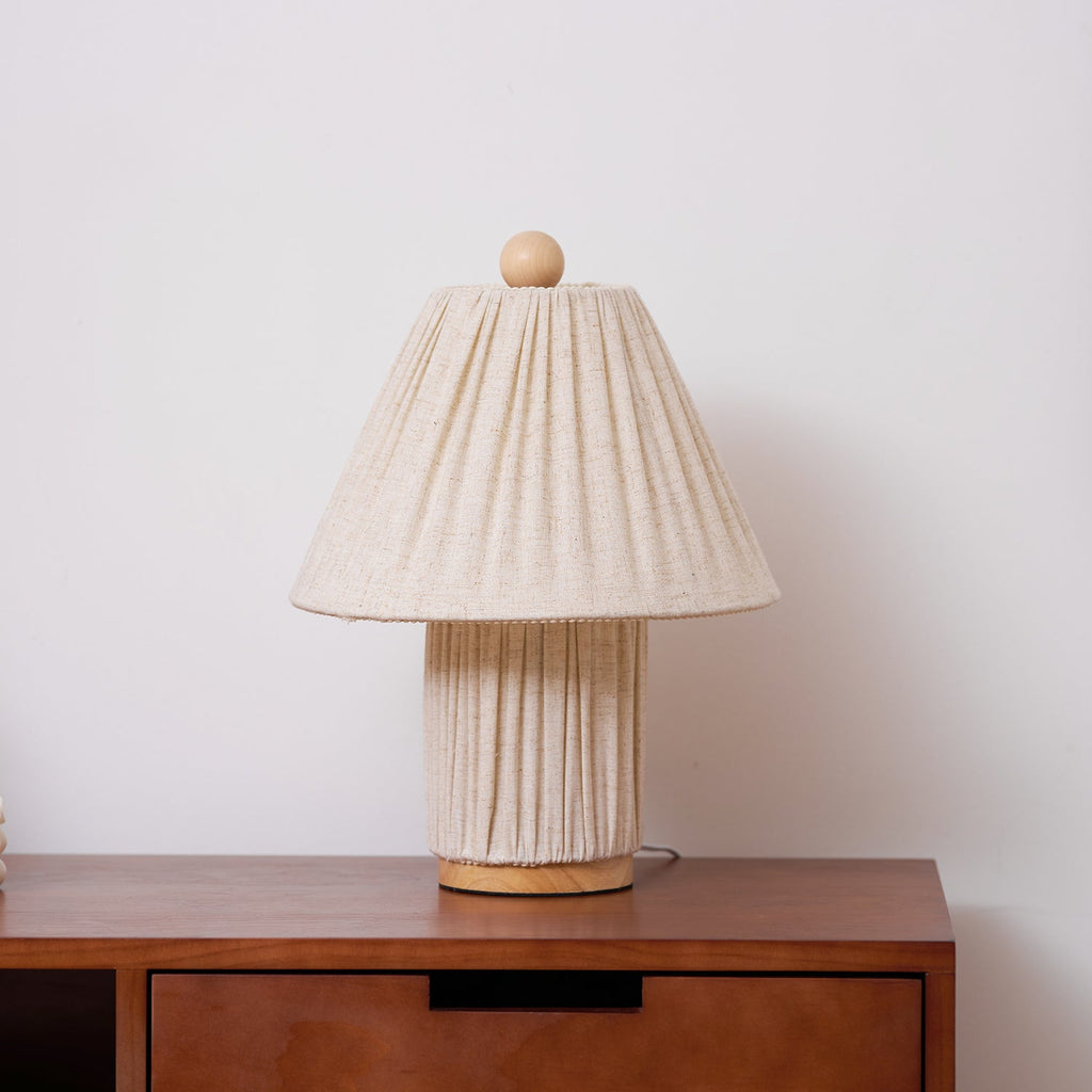 A Clérachic pleated linen lamp stands on a walnut cabinet with a drawer, against a light wall.