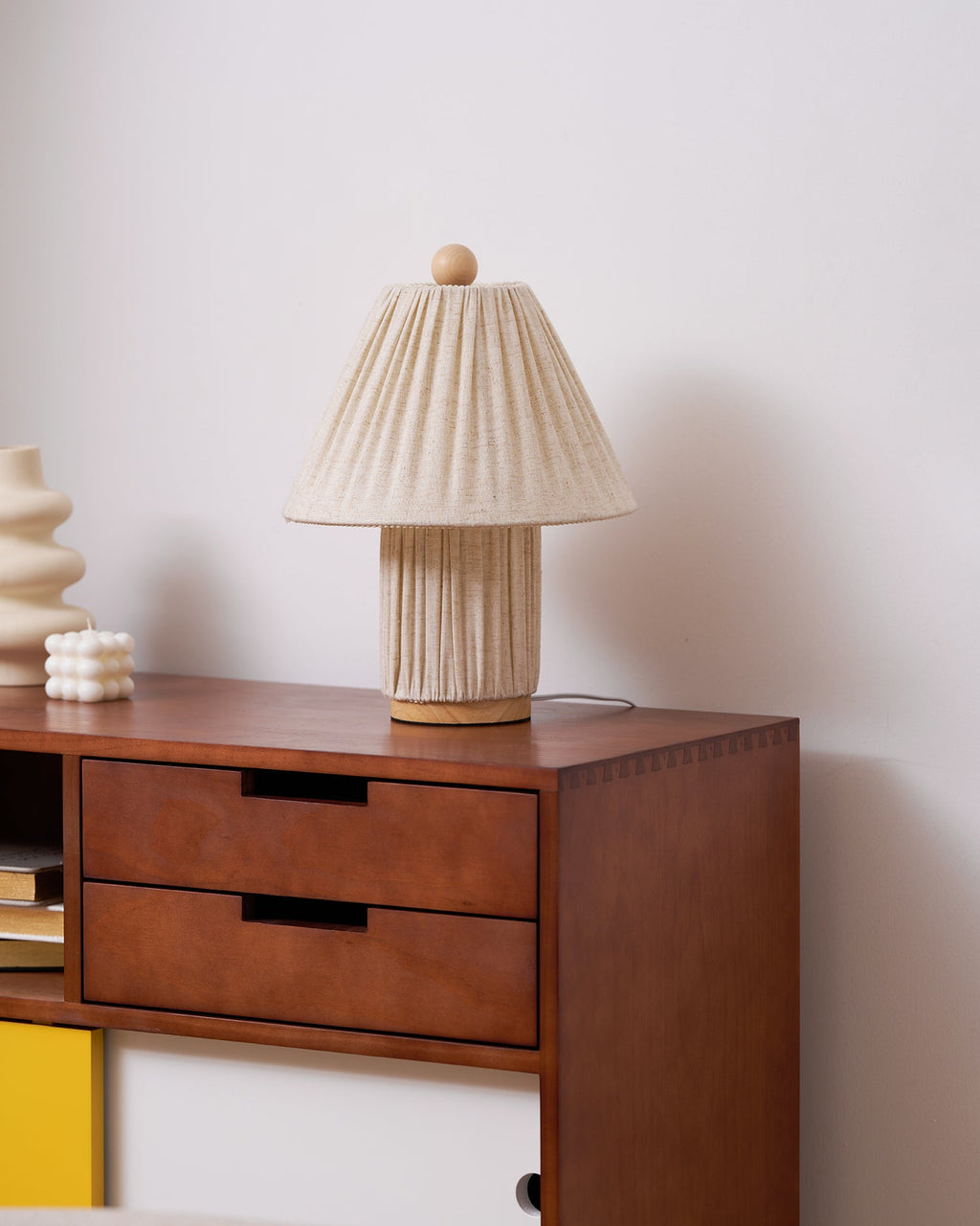 The Clérachic linen lamp, unlit, on a walnut sideboard, with a cream vase and a small bobbled candle beside it.
