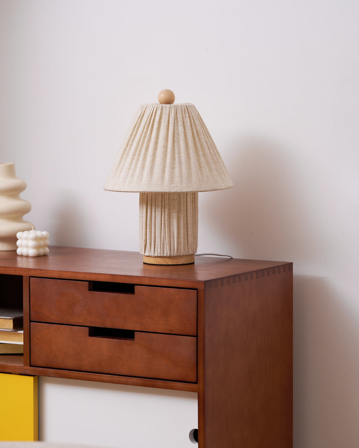 The Clérachic linen lamp, unlit, on a walnut sideboard, with a cream vase and a small bobbled candle beside it.