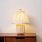 Warm light shines through the pleated linen shade of this Clérachic lamp, set on a walnut cabinet against a pale wall.