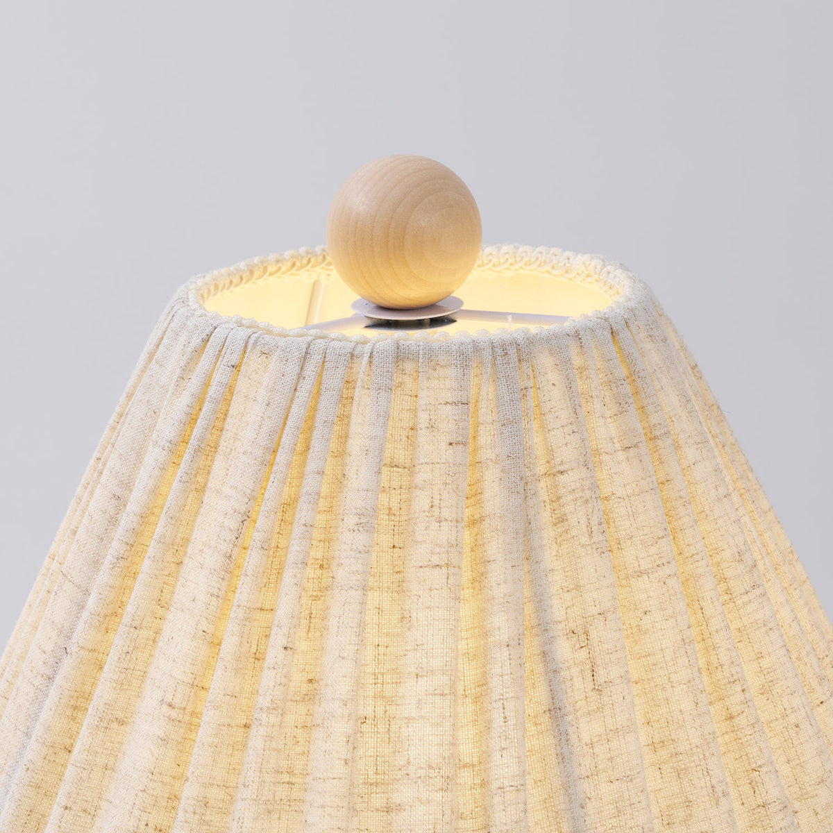 Close view of the wooden ball finial and gathered top edge of the linen shade on this Clérachic lamp.