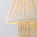 Close view of the pleated linen shade over the matching pleated base on this Clérachic lamp, lit softly from inside.