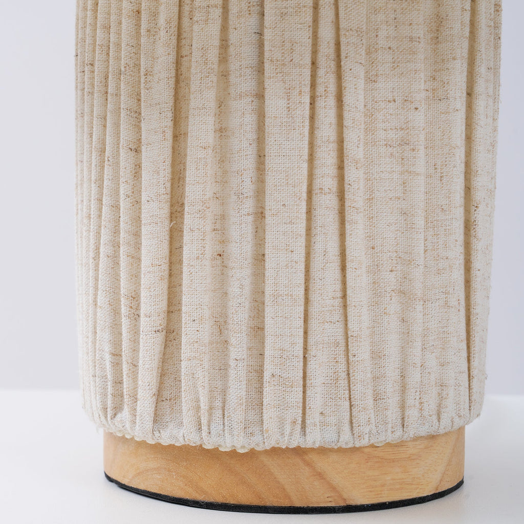Close view of the pleated fabric base of this Clérachic lamp, gathered at the bottom around its round wooden foot.