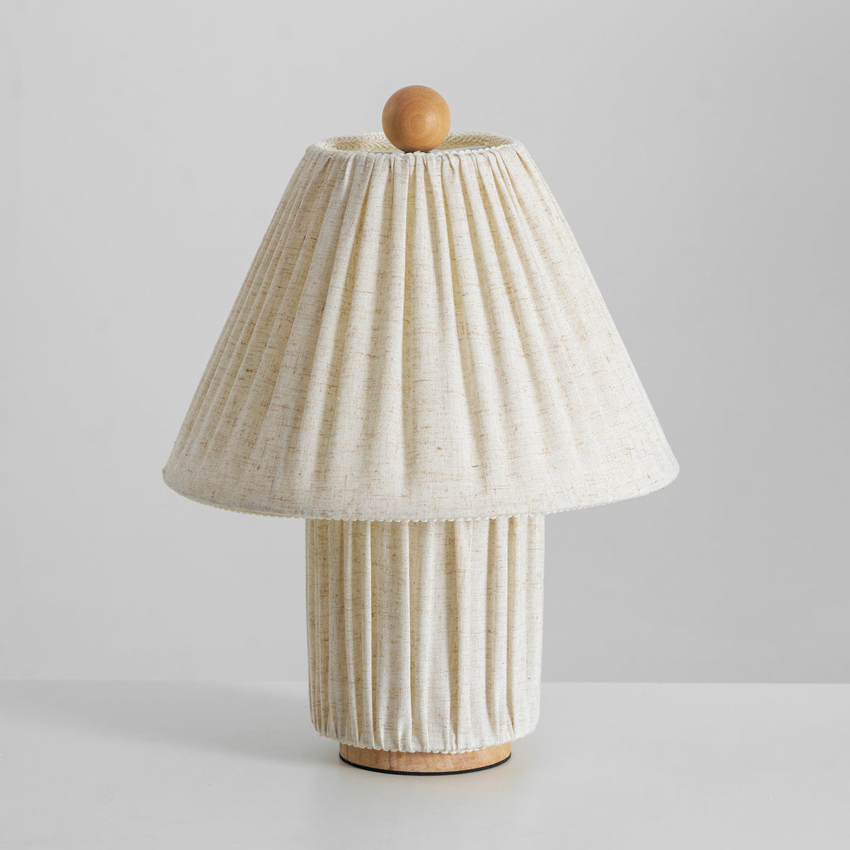 Unlit Clérachic linen lamp with a pleated shade, a matching base and a wooden ball finial, on a pale grey surface.