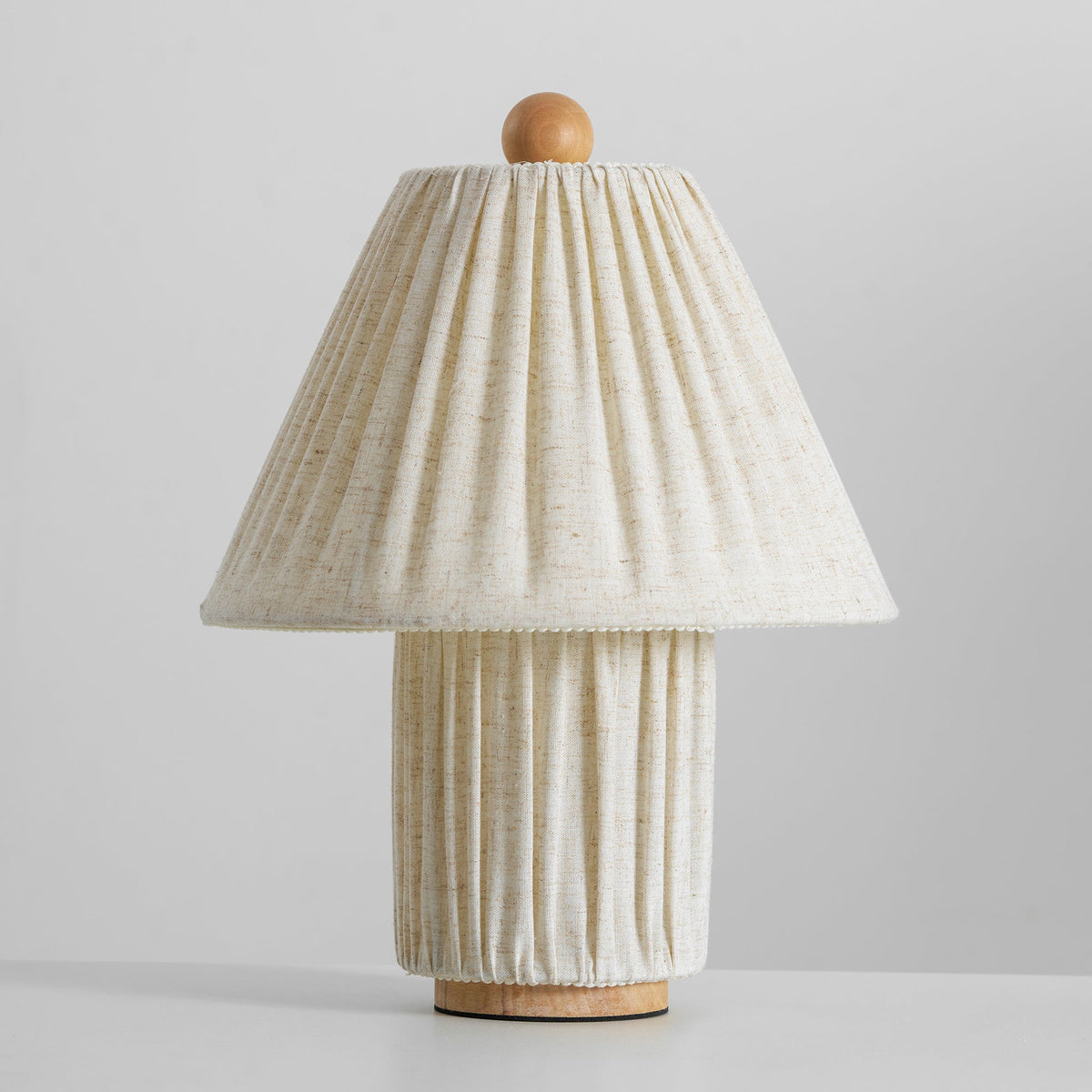 Front view of an unlit Clérachic linen table lamp, its pleated shade slightly closer to the camera, on a pale grey surface.