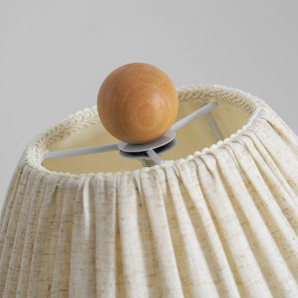 Close view of the wooden ball finial and the gathered top of the linen shade on this Clérachic lamp, with the bulb mount inside.