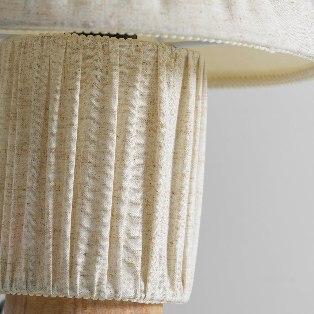Close view of the linen-coloured pleated base of this Clérachic lamp, with the shade's hem overhead.