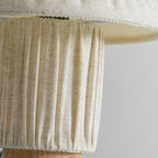 Close view of the linen-coloured pleated base of this Clérachic lamp, with the shade's hem overhead.