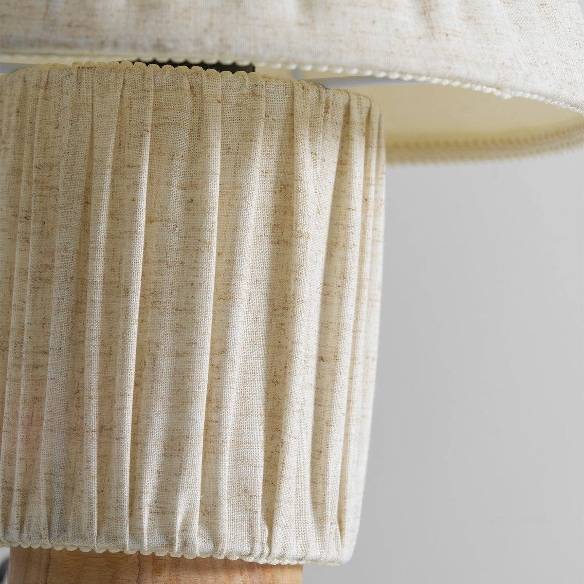 Close view of the linen-coloured pleated base of this Clérachic lamp, with the shade's hem overhead.