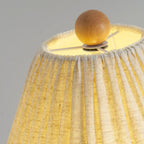Close view of the lit top of a linen Clérachic lamp shade, with the wooden ball finial and the bulb glow inside.