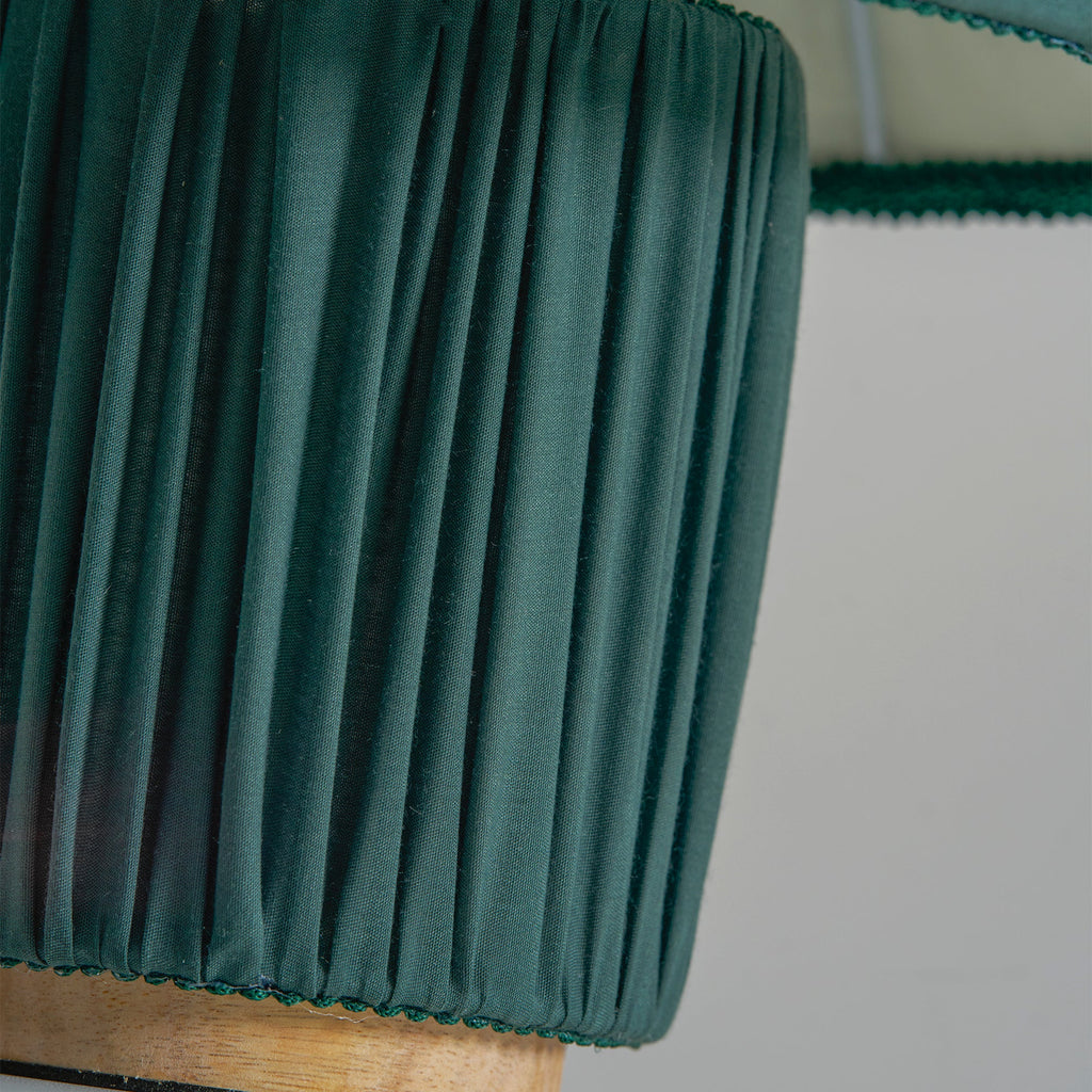 Close view of the dark green pleated base of this Clérachic lamp, with its wooden foot below.