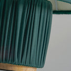 Close view of the dark green pleated base of this Clérachic lamp, with its wooden foot below.