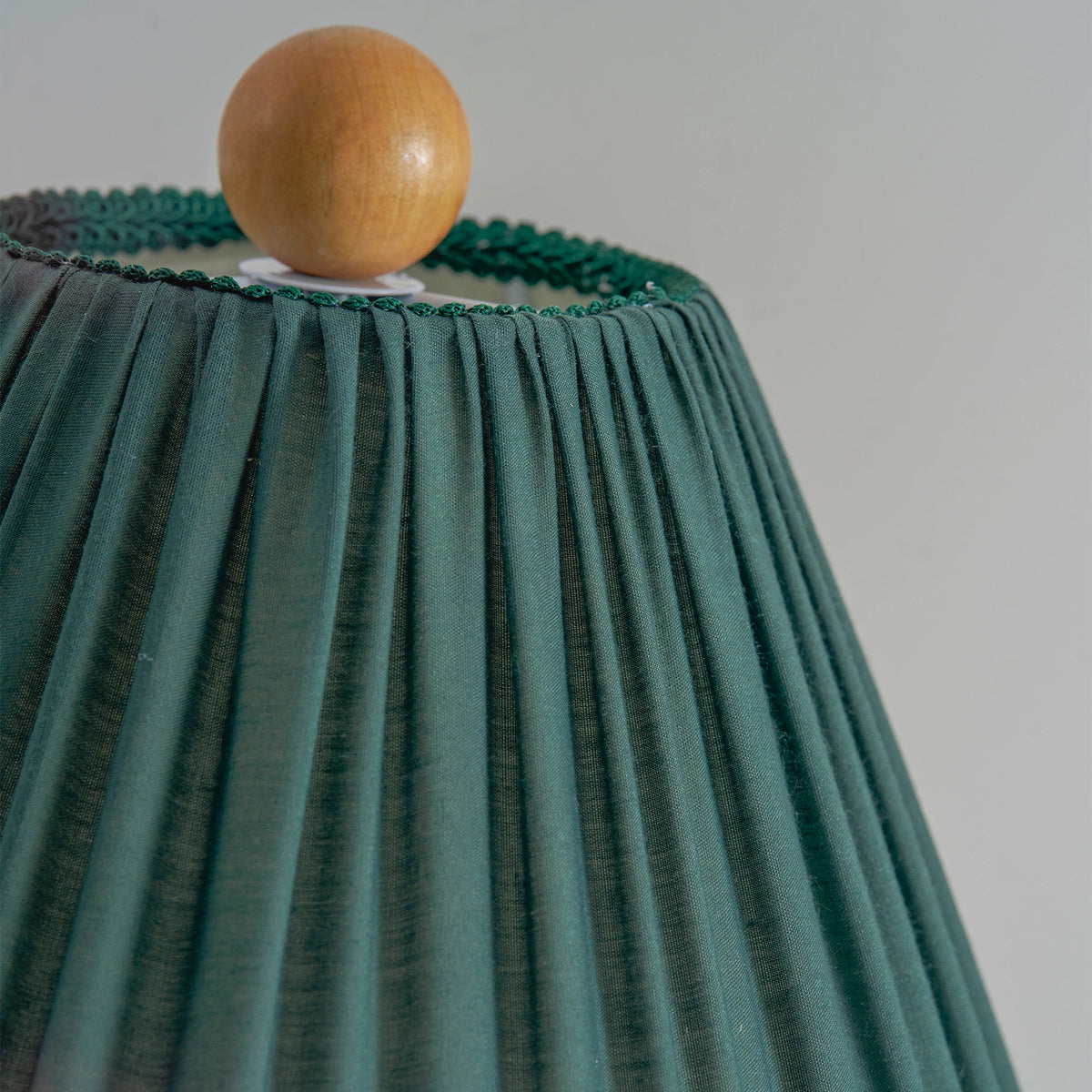Close view of the dark green pleated shade of this Clérachic lamp, with the wooden ball finial and a green edge trim.