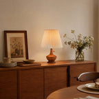 Clérachic table lamp on a wooden sideboard in a warm room, beside a framed print, a vase of wildflowers and a stack of plates.